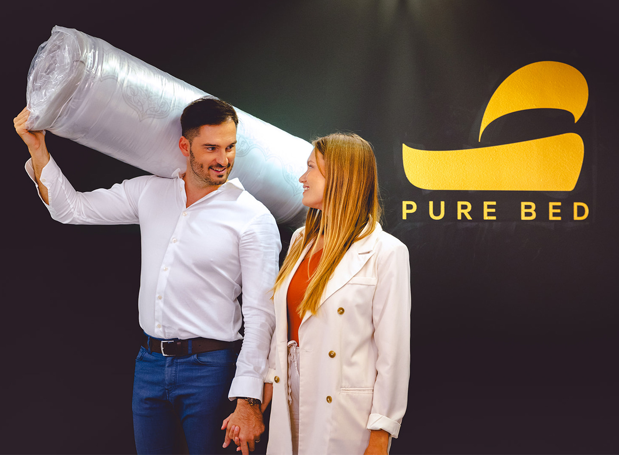 Par v trgovini Pure Bed; moški na rami nosi rolo vzmetnico.